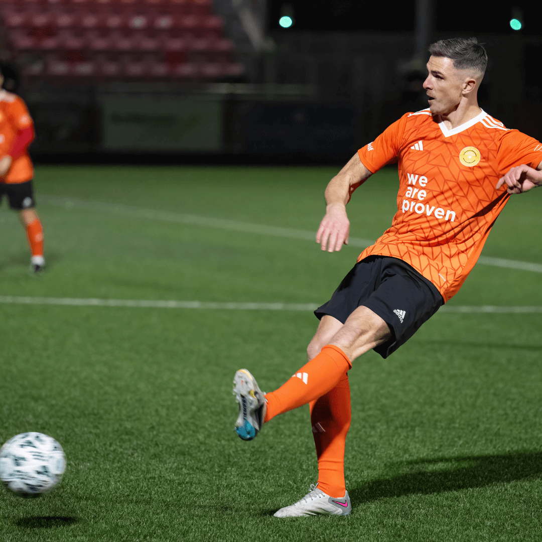 Ciaran Clark in orange kit performing a kick during a football match under stadium lights.